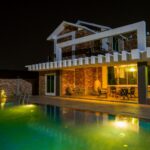 A stunning modern house exterior with a beautifully illuminated swimming pool at night.