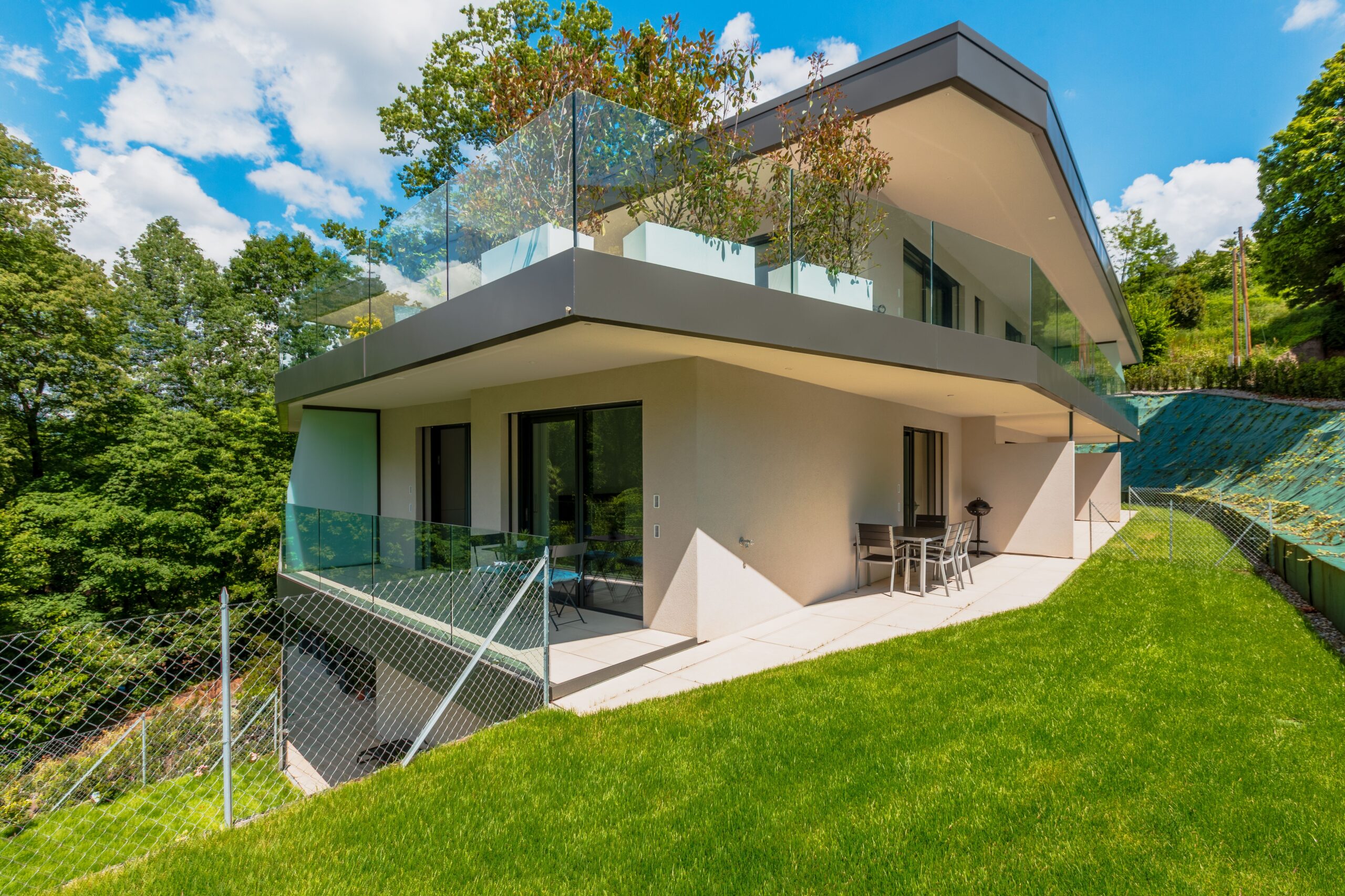 Stunning modern two-story home featuring glass railing and lush surroundings.